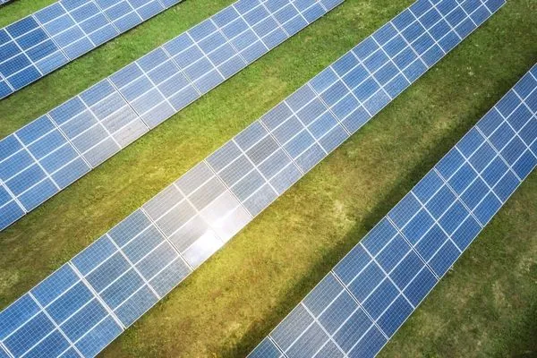 Aerial view of rows of solar panels on a grassy field, reflecting sunlight.