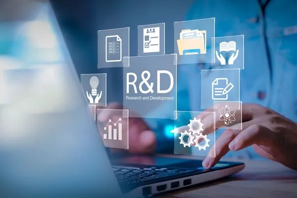 Person typing on a laptop with holographic icons related to research and development, including graphs, documents, and lightbulbs.