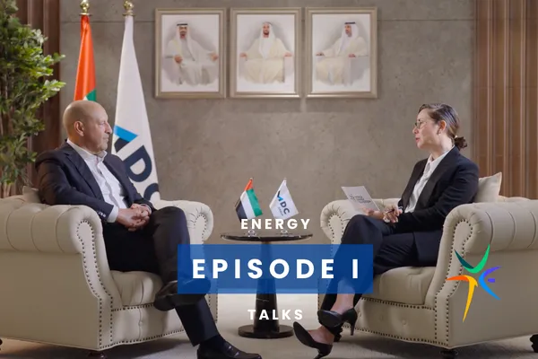 Two people seated in armchairs discussing energy topics, with small flags and framed photos in the background. Text reads "Energy Episode 1 Talks."